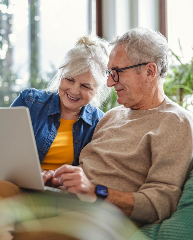 Älteres Ehepaar sitzt gemeinsam auf dem Sofa und nutzt einen Laptop zu Hause.